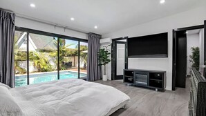 A modern bedroom with a large bed, a TV, and a sliding glass door leading to a pool. - Mansfield Modern - Ultimate Entertainers Oasis With Guest House (Los Angeles)