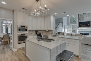 A modern kitchen with white cabinetry, a marble island, stainless steel appliances, and a chandelier. - 5BR Oasis w/ Pool • Steps from Lake Ray Hubbard (Rowlett)
