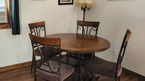 Un comedor con una mesa redonda de madera, cuatro sillas y dos cuadros en la pared.