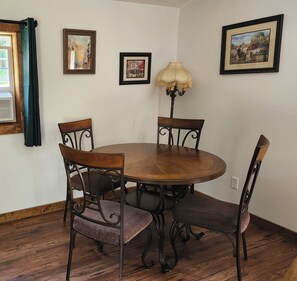 A dining area with a round wooden table, four chairs, and two framed pictures on the wall.