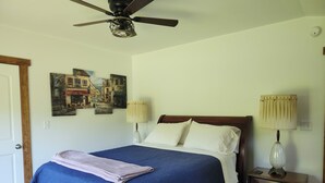 Un dormitorio con una cama, dos lámparas de noche, un ventilador de techo y un cuadro en la pared.