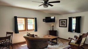 Una sala de estar con ventilador de techo, televisor, mesa de centro de madera, sofá, sillón y alfombra.