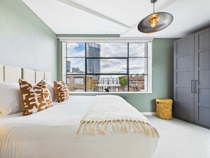 A modern bedroom with a large bed, a view of the city through a large window, and a ceiling light fixture. - Spacious Two-Bedroom Haven by Tech City (Greater London)