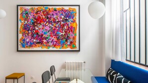 A modern living room with a large abstract painting, a glass dining table, a blue sofa, and a white radiator. - Luxury Apartment 4br/8p - Notre Dame / Bastille (Paris)