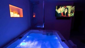 A room with a bathtub, a television, and a small shelf with candles. - Intimate Flat w/ A/C & Jacuzzi - 2br/6p Montmartre (Paris)