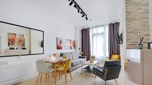 A modern living room with a dining area, a grey sofa, yellow chairs, and a black armchair. There are two abstract paintings on the walls and a large window with curtains. - Intimate Flat w/ A/C & Jacuzzi - 2br/6p Montmartre (Paris)