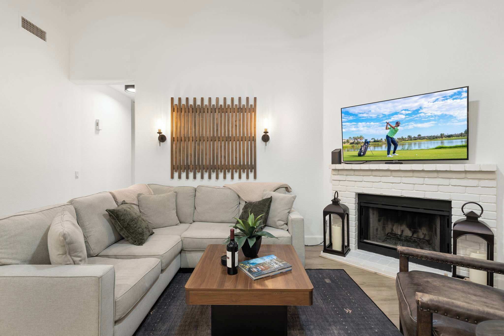 A living room with a sectional sofa, a coffee table, a flat-screen TV, a fireplace, and a wall-mounted light fixture.