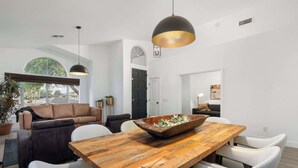 A modern living room with a wooden dining table, white chairs, a brown sofa, and a black pendant light. - Pool| Lake Views |Private Dock |Paddleboat |Oasis (Glendale)