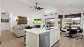 A modern kitchen with a dishwasher, a dining area with a round table and chairs, a sofa, and a ceiling fan. - Pool| Lake Views |Private Dock |Paddleboat |Oasis (Glendale)