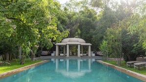 Una piscina con un pabellón en el centro, rodeada de abundante vegetación.