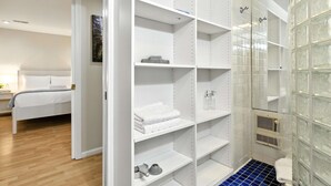 Siisti hotellihuone, jossa on järjestelmällinen vaatekaappi, lasiseinällä varustettu suihkutila ja valkoisella päätyosalla varustettu sänky.