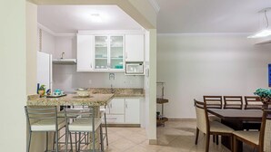 A kitchen with white cabinets, a granite countertop, and a dining area with wooden chairs and a table. - Apart w Barbecue Grill 180m From the Beach Cgb0035 (Ubatuba)