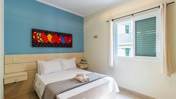 A bedroom with a bed, a nightstand, a wall art piece, a window with curtains, and a tiled floor.
