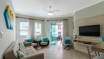 Un salon avec un canapé, des fauteuils, un téléviseur et un balcon agrémenté de rideaux.