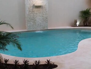 Una piscina con un muro de piedra y palmeras.