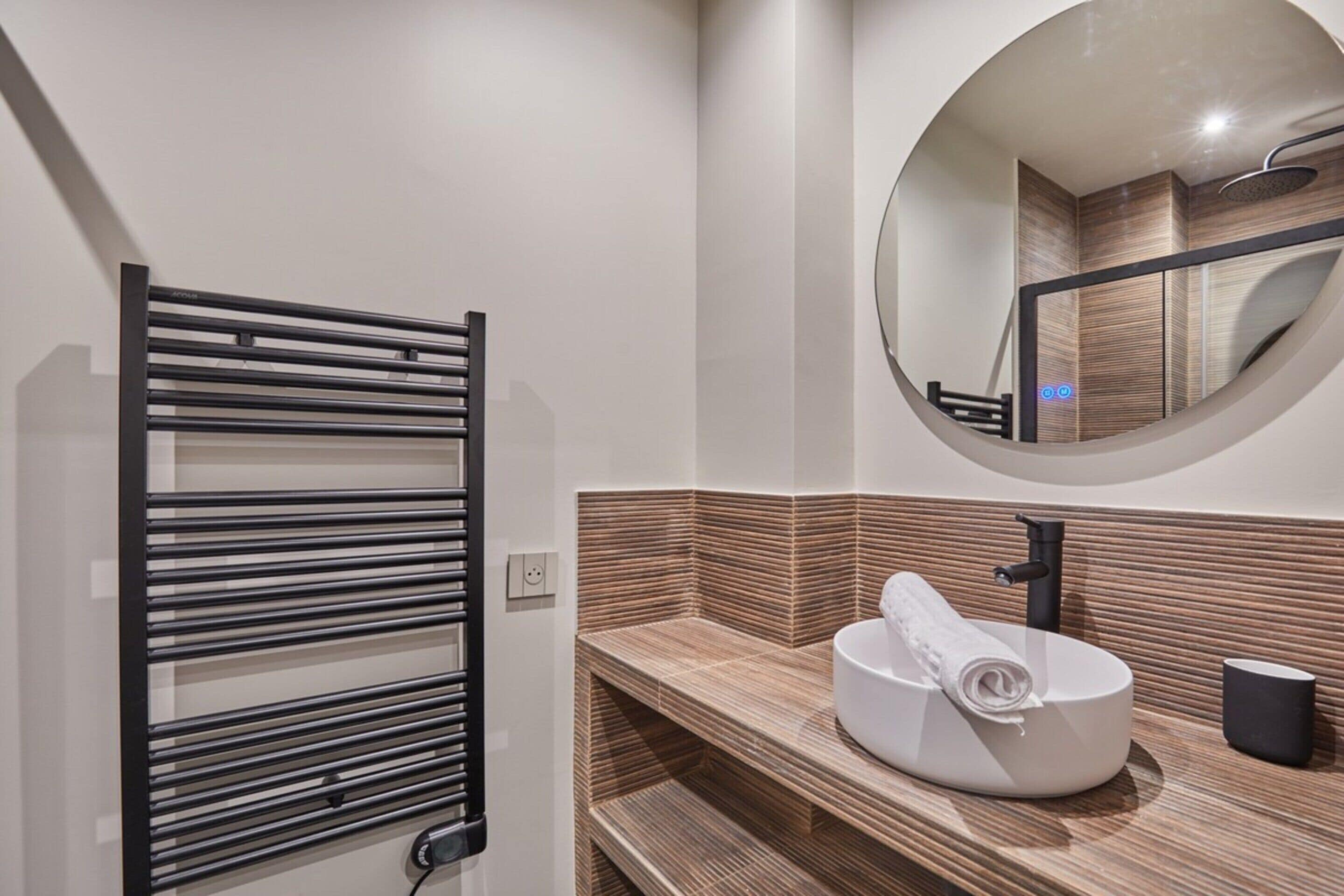 A modern bathroom with a towel rack, a sink with a mirror above it, and a wooden textured wall.