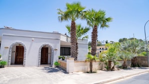 A modern building with two arched doorways and a balcony with potted plants. - Villa Sardinella-5 Bedroom Villa With Private Pool (Mellieha)