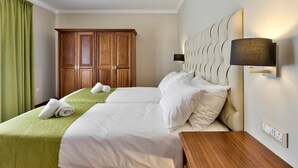 A hotel room with two beds, a wooden wardrobe, a wall-mounted lamp, and a green curtain. - Villa Hibiscus 3 Bedroom Villa With Private Pool (Mellieha)