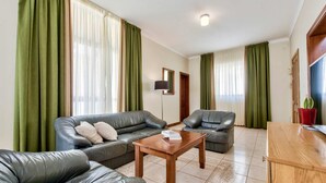 A living room with leather sofas, a wooden coffee table, and green curtains. - Villa Hibiscus 3 Bedroom Villa With Private Pool (Mellieha)