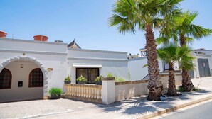 A white building with arched doorways, a gated entrance, and palm trees. - Villa Hibiscus 3 Bedroom Villa With Private Pool (Mellieha)