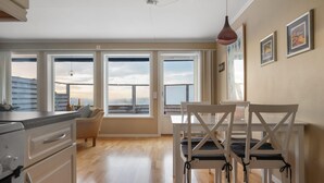 Een ruime keuken met grote ramen, een eetgedeelte met witte stoelen en uitzicht op zee.