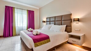 A hotel room with a large bed, a nightstand, and a wall-mounted lamp. - Villa Stephanotis - 3 Bedroom Villa With Pool (Mellieha)