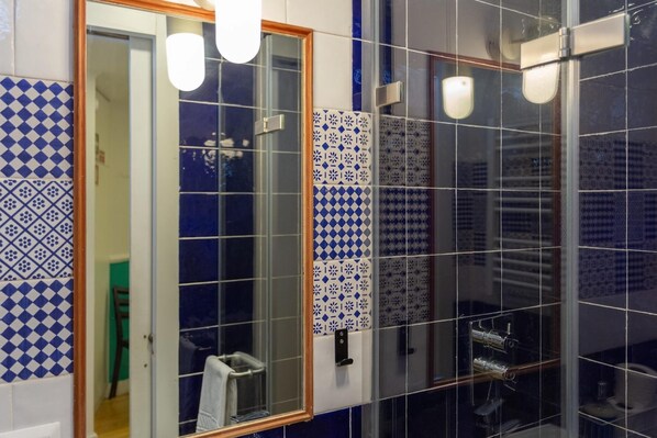 Un baño con baldosas estampadas, mampara de vidrio y un perchero visible.