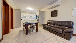Una sala de estar con un sofá de cuero marrón, una mesa de comedor con sillas y una cocina al fondo.