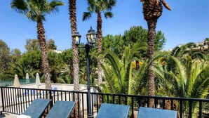 Zona de piscina con sillones de descanso y palmeras.