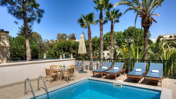 Un área de piscina con sillones, una mesa y vistas a palmeras y edificios.