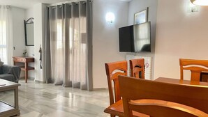 Una sala de estar moderna con comedor, un televisor de pantalla plana en la pared y un ventanal corredero que da a un balcón.
