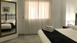 Habitación de hotel con cama, mesita de noche con lámpara, espejo y ventana con cortinas.