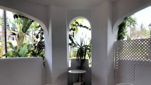 Un comedor con una mesa y sillas, rodeado de paredes blancas y ventanas amplias con plantas.