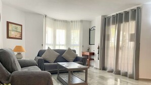 Una sala moderna con un sofá gris, una mesa de centro y una lámpara. También hay una pequeña mesita de madera y una planta en maceta.