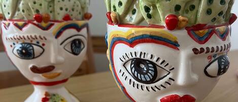 Deux vases en céramique ornés de visages, l’un avec un œil bleu et l’autre avec un œil rouge, sont posés sur une surface en bois.