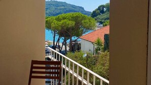 A balcony with a wooden chair and a table, overlooking a coastal area with trees and buildings. - Rebecca s Portovenere Collection (Portovenere)