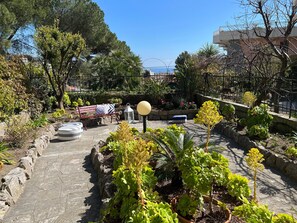 Un jardín con un camino de piedra, un banco rojo y diferentes plantas en macetas.