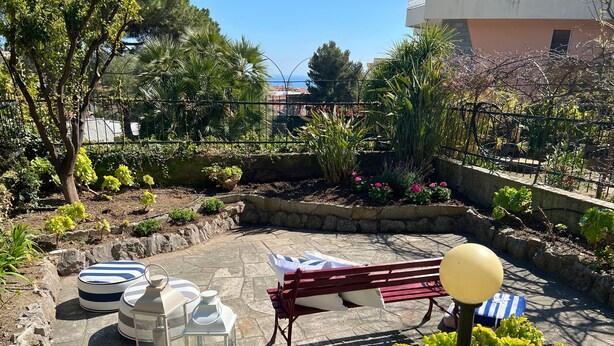 An outdoor patio area with a red bench, a table with a white tablecloth, and various potted plants. - Rebecca s Sanremo Collection I (Sanremo)