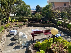 An outdoor patio area with a red bench, a table with a white tablecloth, and various potted plants. - Rebecca s Sanremo Collection I (Sanremo)