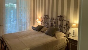 A bedroom with a bed, two bedside tables, and a window with sheer curtains. - Rebecca s Sanremo Collection I (Sanremo)