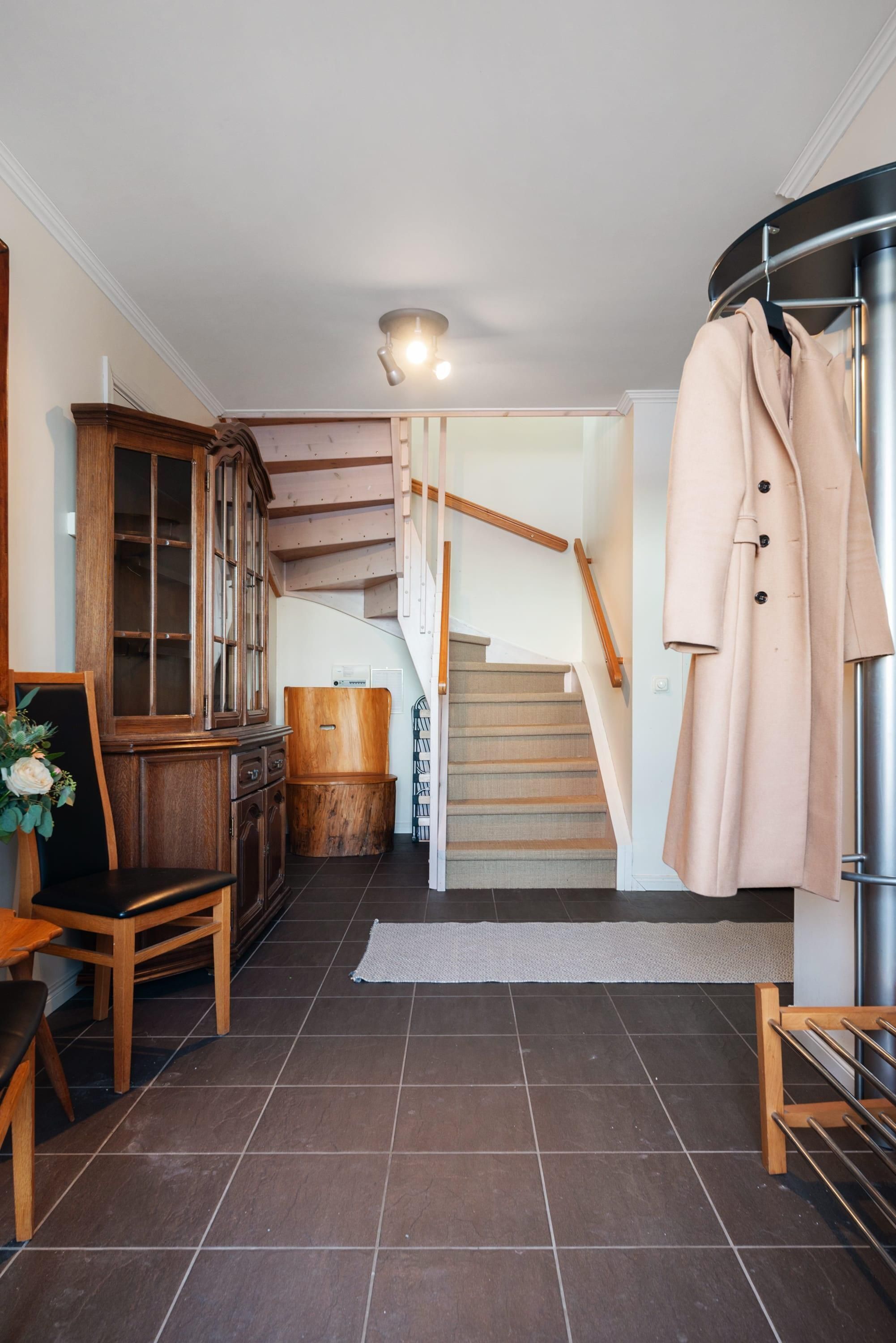 Eine Treppe führt zu einer zweiten Etage, mit Holzgeländer und einem Kleiderhaken rechts.