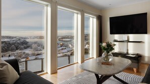 A spacious living room with large windows, a flat-screen TV, and a view of a lake and buildings. - Vetteberget Huset in Fj Llbacka (Fjallbacka)