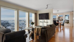 A spacious living room with large windows, a flat-screen TV, and a dining area. - Vetteberget Huset in Fj Llbacka (Fjallbacka)