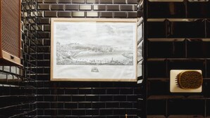 Un baño con paredes de azulejos negros, un cuadro en la pared, un inodoro y un lavabo.