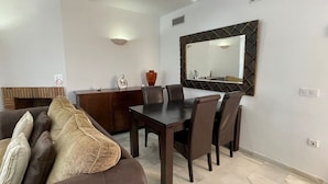 Ein Essbereich mit dunklem Holztisch und Stühlen, einem braunen Sofa mit Kissen, einem Holzschrank und einem an der Wand befestigten Spiegel.