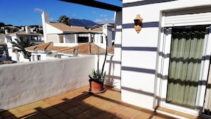 Ein Balkon mit Terrakottafliesen, einem Blumentopf und einer weißen Wand mit Fenster und einer Wanddekoration.