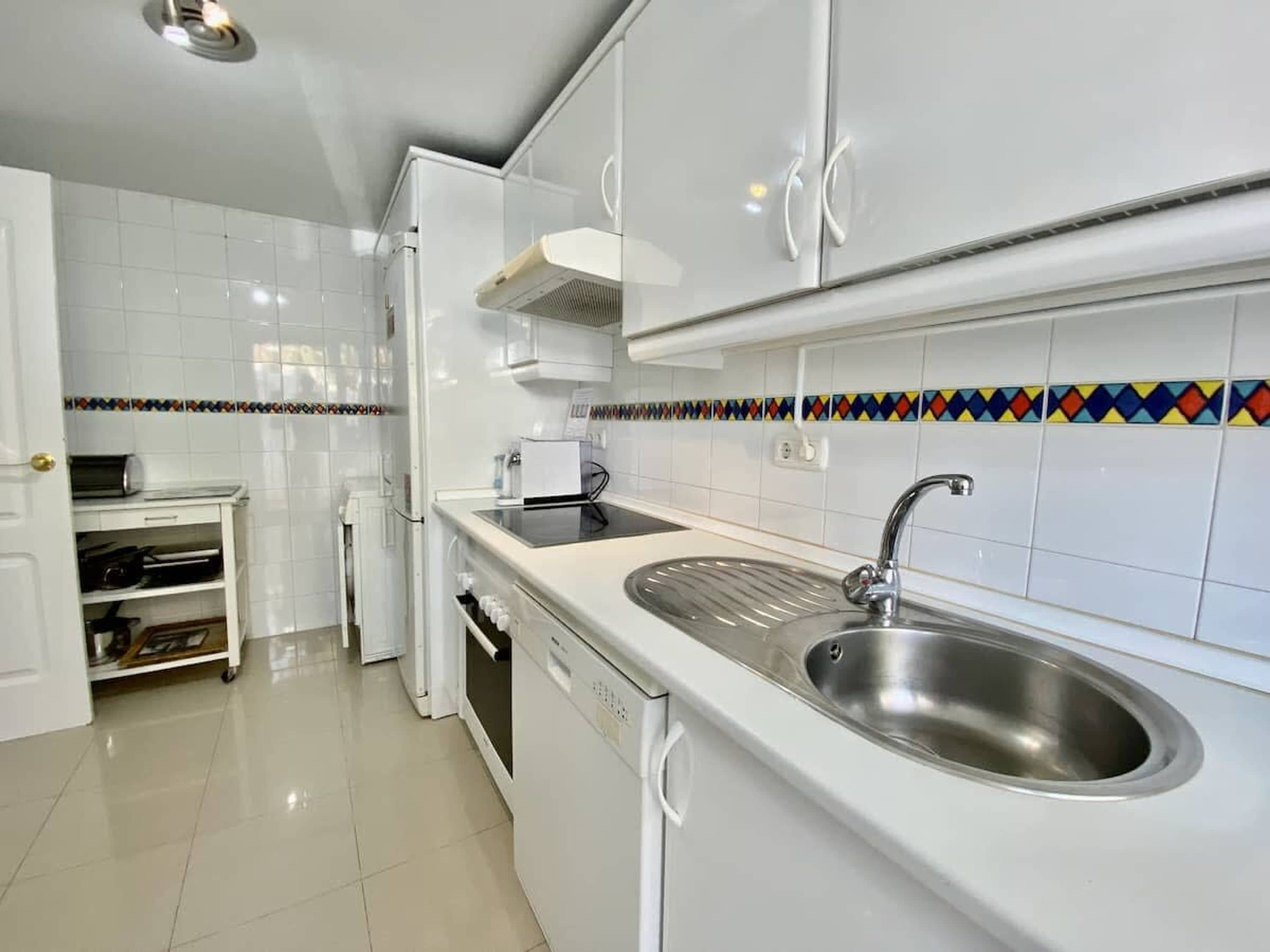 Una cocina moderna con armarios blancos, un lavamanos de acero inoxidable y un salpicadero de azulejos de colores.