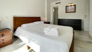 A neatly made bed with white linens and towels, a wooden headboard, a nightstand with a lamp, and a painting on the wall.
