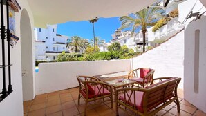A balcony with a table and chairs, overlooking a residential area with white buildings and palm trees. - Spacious Poolside 3 Bedroom F-5 (Marbella)