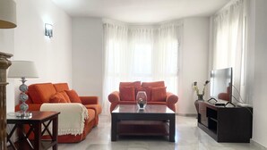 A living room with two orange sofas, a coffee table, a TV, and a lamp. - Spacious Poolside 3 Bedroom F-5 (Marbella)